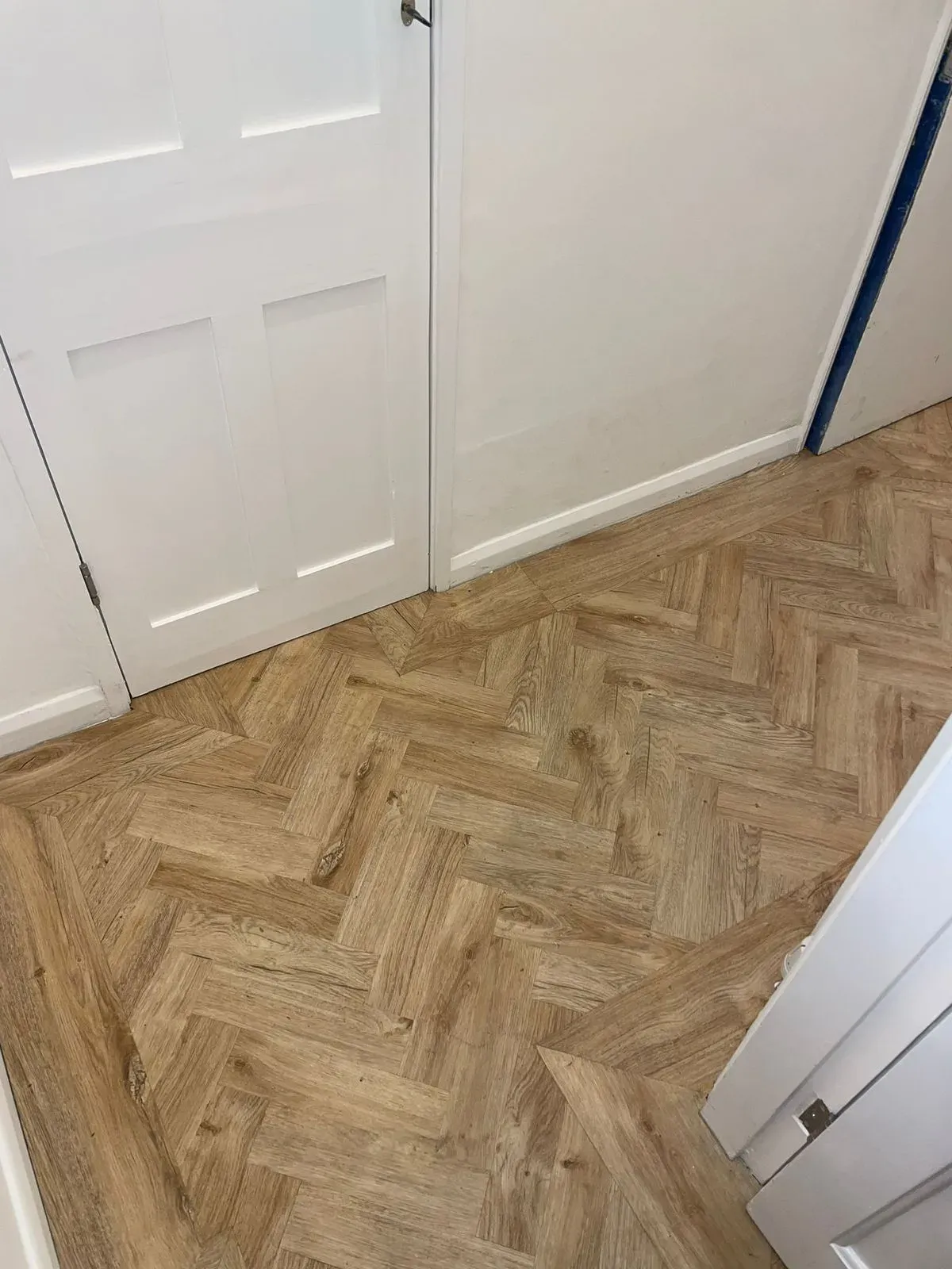 White internal door and skirting boards beside herringbone flooring.