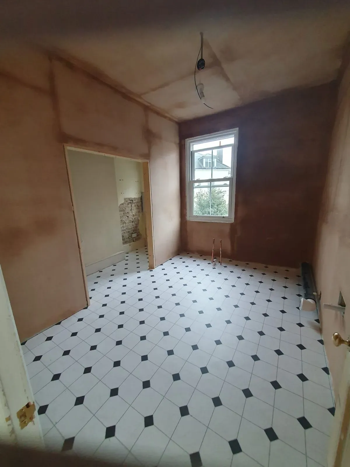 Freshly plastered walls and ceiling in a room with a window and patterned flooring.
